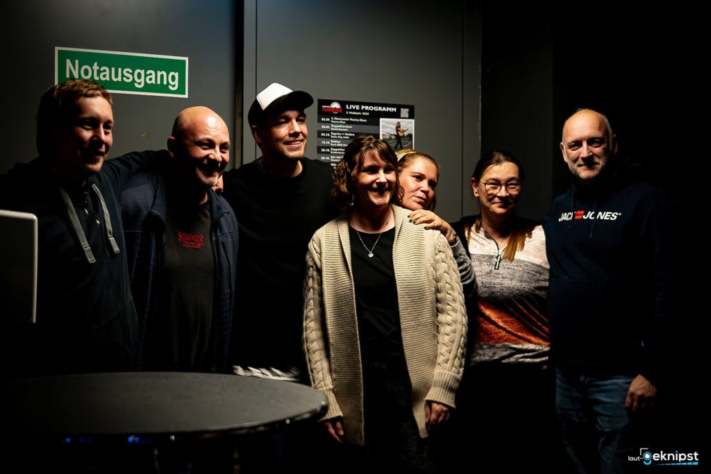 Gruppe lächelnder Menschen vor einer Notausgangstür.