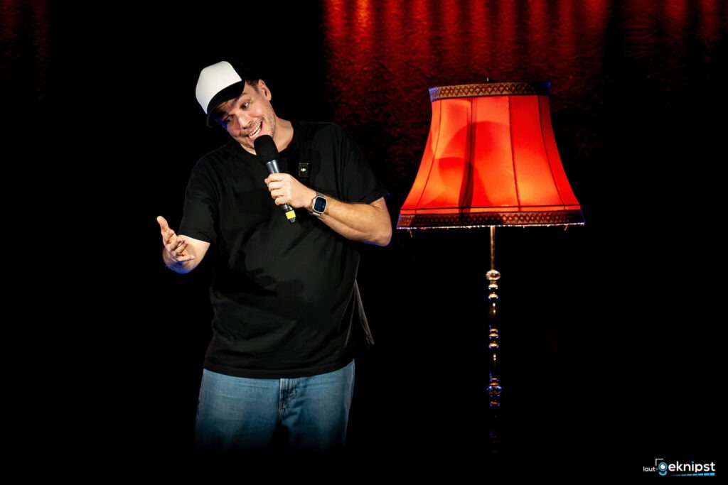 Mann auf Bühne mit roter Stehlampe