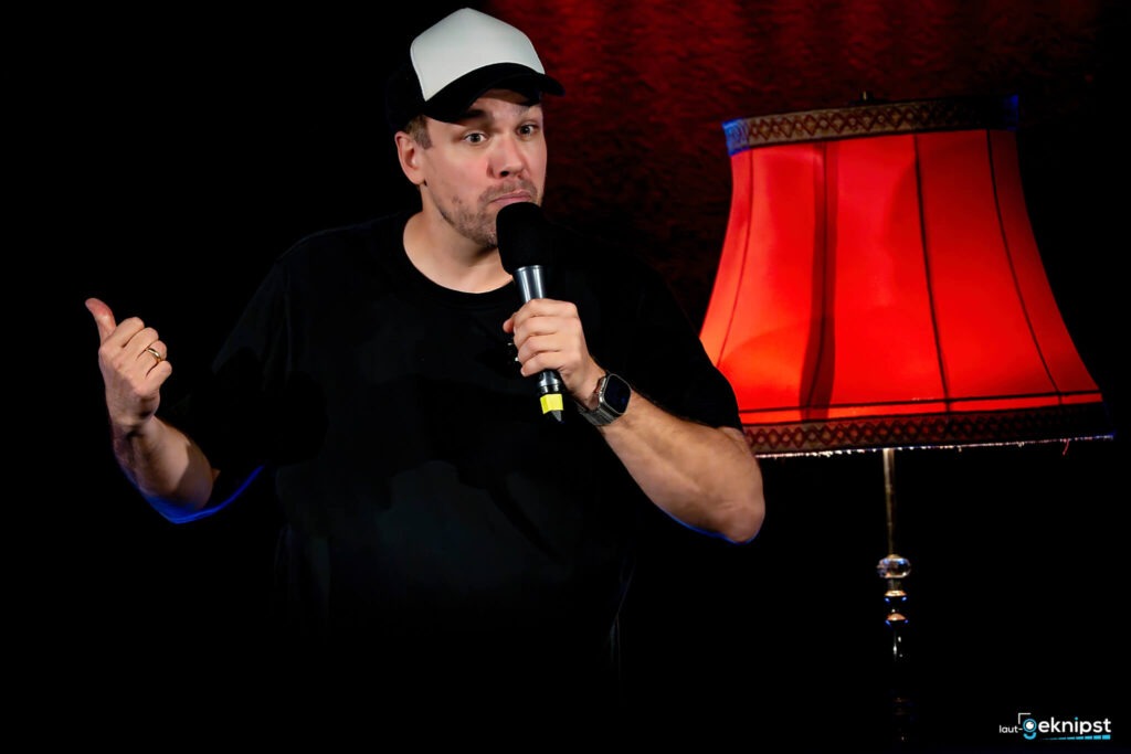 Komiker auf Bühne mit roter Lampe im Hintergrund.