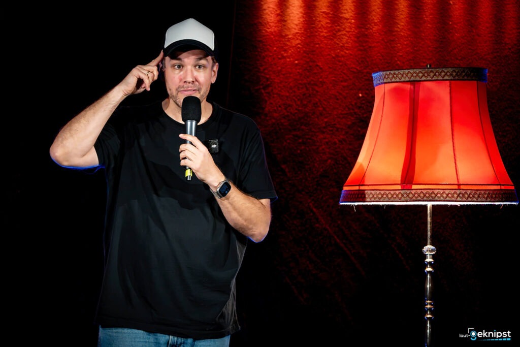 Mann mit Mikrofon und roter Lampe auf Bühne.