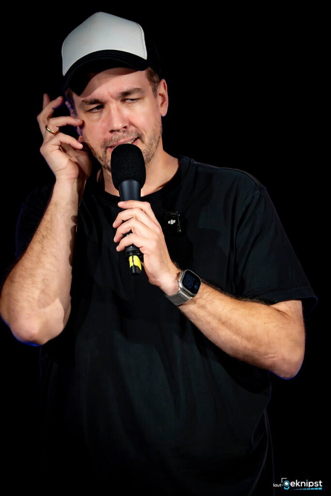 Mann mit Mikrofon und Baseballkappe auf der Bühne.