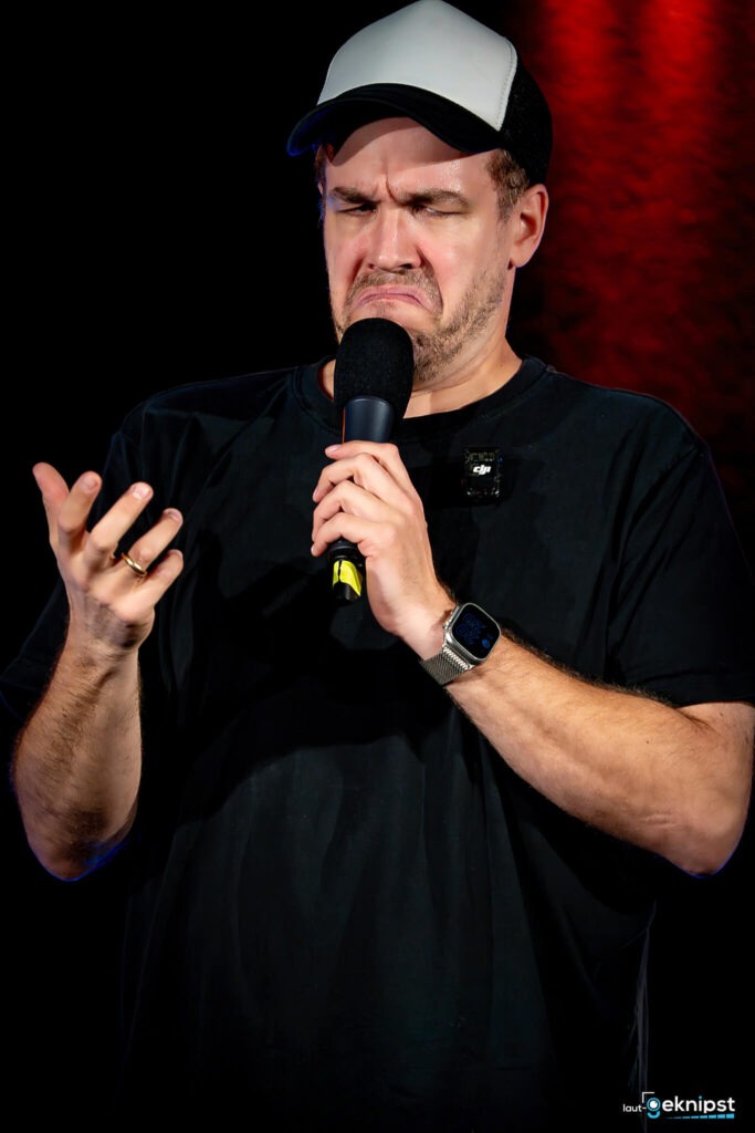 Mann mit Mikrofon zeigt angewiderten Ausdruck.