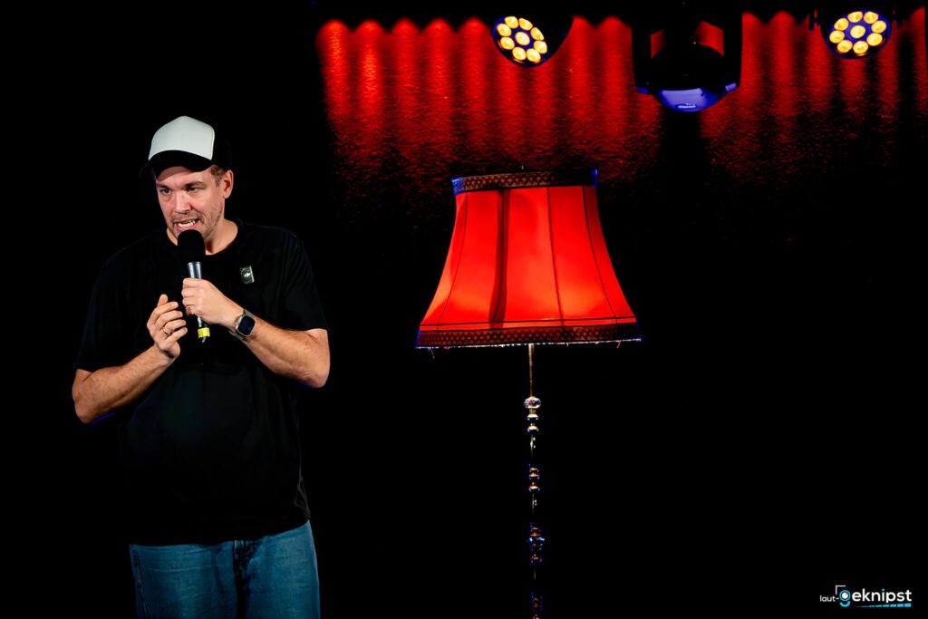 Mann mit Mikrofon neben roter Stehlampe