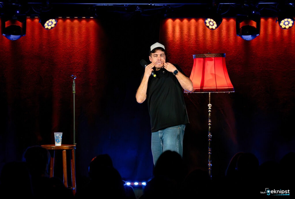 Comedian auf Bühne mit Stehlampe und Mikrofon.