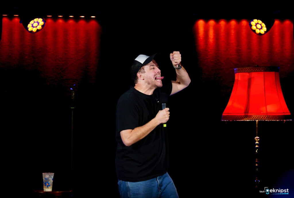 Komiker auf Bühnenperformance mit rotem Lampenschirm.