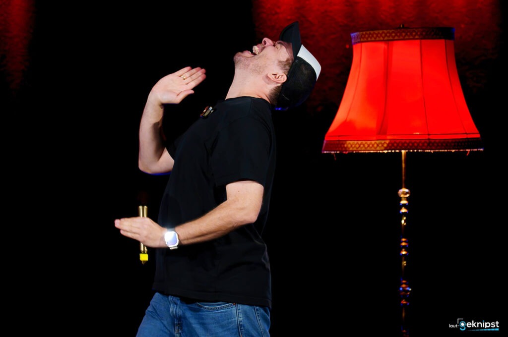 Mensch lacht unter einer roten Lampe auf Bühne.