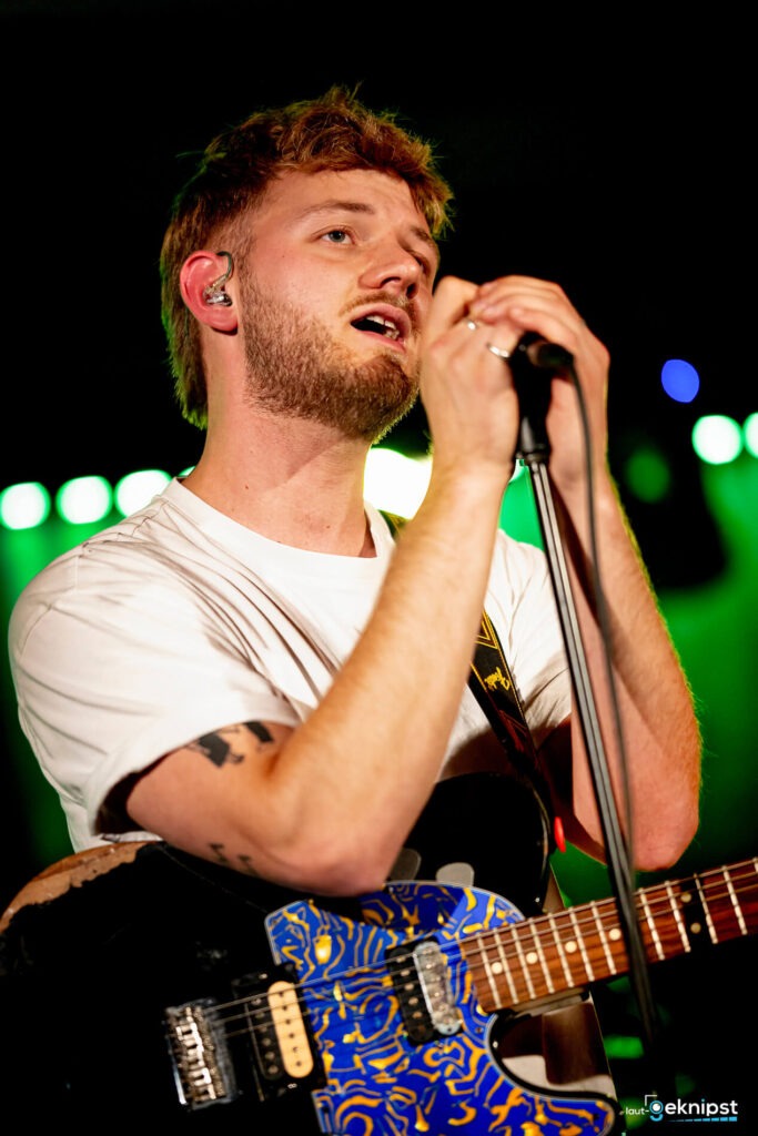 Musiker singt auf Bühne mit bunter Gitarre.