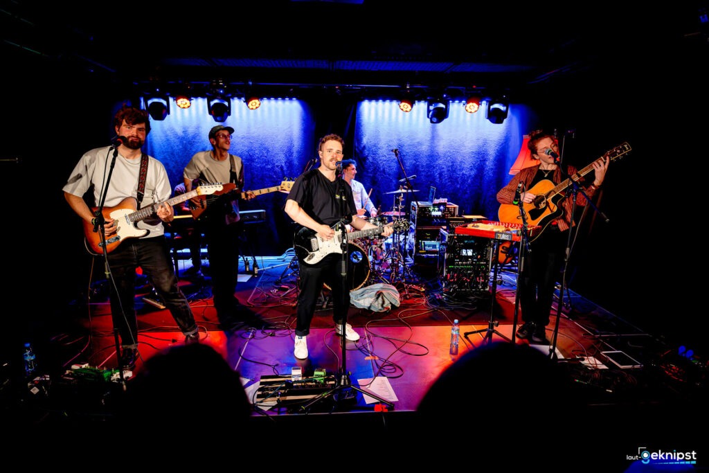 Band auf der Bühne mit Instrumenten und Lichtern.