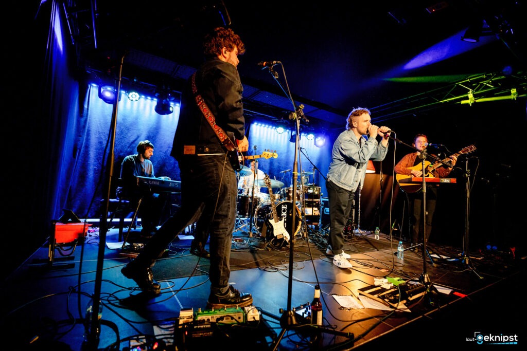 Band spielt live auf Bühne mit blauer Beleuchtung.