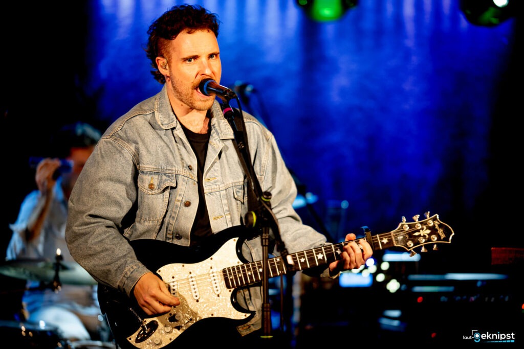Musiker singt und spielt E-Gitarre auf Bühne.